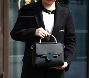 Detail of black lychee grain leather bag with circular metal buckle and round metal handle