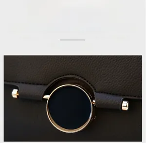 Detail of a dark gray leather bag featuring a polished gold circular metal clasp buckle