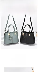 Detalle del bolso de mano estructurado en verde oscuro y negro con colgante de trébol