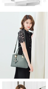 Detalle de bolso verde salvia con colgante de trébol y costuras decorativas