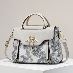 Close-up of golden swan buckle with pearl charms on paisley printed leather handbag