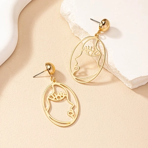 Boucles d'oreilles dorées au design de visage abstrait sur un présentoir en pierre