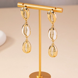 Chic triple-layered gold seashell drop earrings with white enamel on a jewelry stand