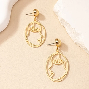 Détail de boucles d'oreilles dorées avec visage abstrait et silhouette artistique