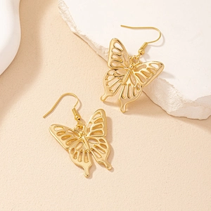 Elegant gold hollow butterfly drop earrings on stone textured prop with soft lighting