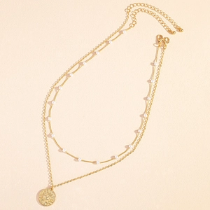 Dettaglio della collana a due strati dorata con perle bianche e ciondolo a sole su sfondo