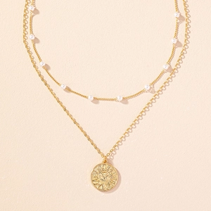 Dettaglio di una collana dorata a due strati con perle e ciondolo a sole
