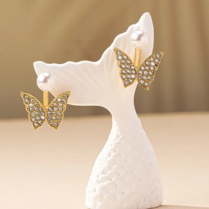 Boucles d'oreilles papillon dorées avec perles et cristaux sur support à bijoux