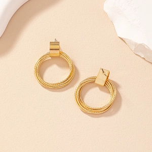 Detailed view of layered golden geometric hoop earrings on textured beige stone surface