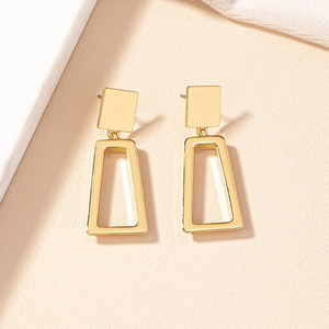 Modern geometric square and hollow trapezoid gold earrings on a minimalist beige base