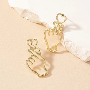 Golden finger heart stud earrings with hollow heart detail on white stone texture