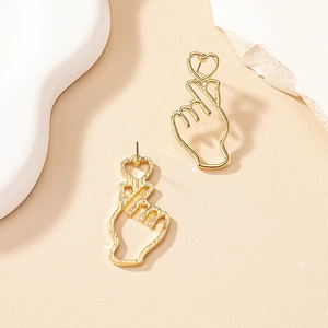 Detail of gold finger heart gesture earrings with textured matte finish on warm background