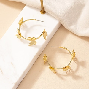 Boucles d'oreilles créoles dorées ornées de papillons détaillés sur fond de marbre