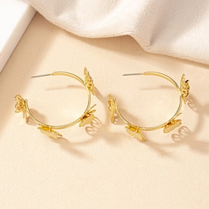 Boucles d'oreilles créoles dorées avec breloques papillons sur un tissu texturé