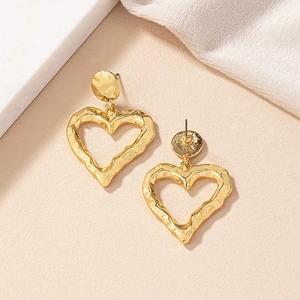 Detail of gold hollow heart earrings showing irregular hammered metal texture and finish