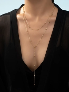 Detail of a layered gold Y-necklace with small beads worn by a model in black clothing