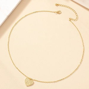 Collier à pendentif cœur doré minimaliste avec détails texturés sur fond beige chaud