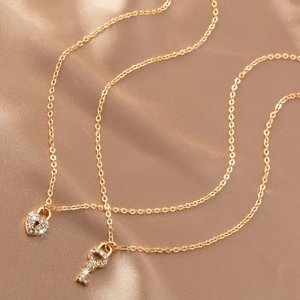 Détail de colliers dorés avec pendentifs cadenas cœur et clé sertis de cristaux