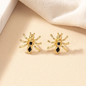 Boucles d'oreilles araignée dorées avec pierres noires sur fond beige texturé élégant