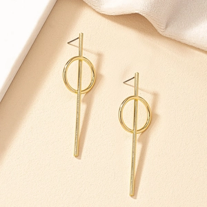 Close-up of golden geometric dangle earrings with circular and linear elements on beige background
