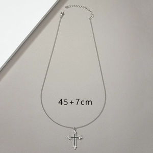 Detail of silver cross pendant with 45+7cm chain length measurement on textured background