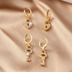 Détails de boucles d'oreilles dorées en forme de cœur et clé serties de strass brillants