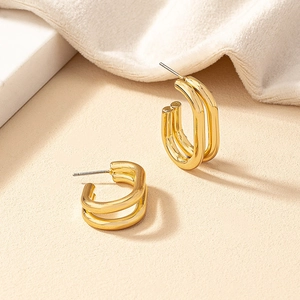 Minimalistische geometrische Doppel-Creolen in Gold auf sandfarbenem Hintergrund