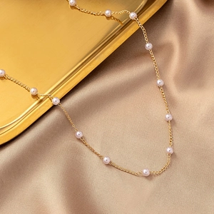 Minimalist gold chain necklace with small freshwater pearls on silk fabric background