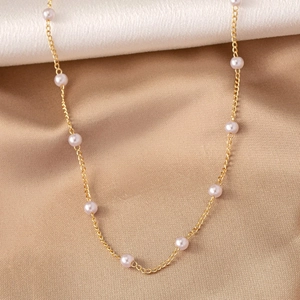 Detail view of a gold chain necklace with small white pearls on silk fabric