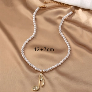 Vue détaillée du collier de perles note de musique avec strass sur fond de satin champagne