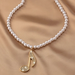 Gros plan d'un collier de perles avec un pendentif note de musique dorée et des cristaux
