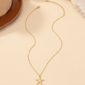 Collier à pendentif étoile de mer dorée avec chaîne fine sur un fond texturé neutre