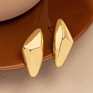 Detail shot of irregular geometric gold stud earrings on a brown porcelain plate edge