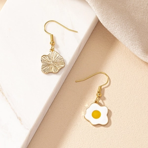 Detail of whimsical fried egg earrings with gold sunburst textured disc on marble surface