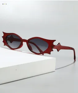 Close-up of deep red bat-shaped sunglasses on a white geometric stand with gradient lenses