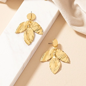 Close-up of golden leaf earrings with hammered texture and layered botanical design
