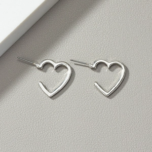 Minimalist silver heart stud earrings with polished finish on grey leather background
