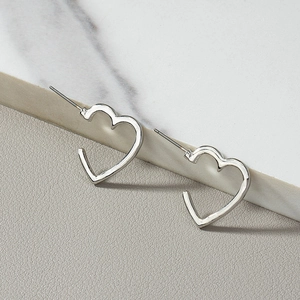 Minimalist silver heart hoop earrings displayed on white marble texture surface