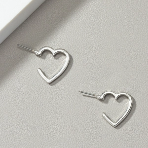 Detail view of hollow heart stud earrings with silver finish on grey textured leather
