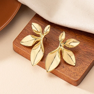 Elegant gold petal leaf earrings with metallic texture on a dark wooden display stand