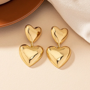 Close-up of golden double heart drop earrings with high-gloss polished metallic finish