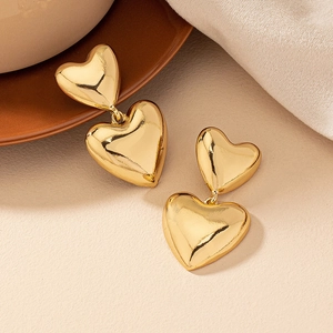 Bohemian double heart gold drop earrings with polished finish on warm knit background
