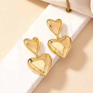 Elegant gold double heart dangle earrings on white marble, minimalist polished jewelry
