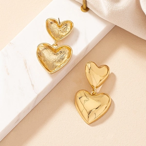 Polished and brushed gold heart drop earrings shown on marble and leather background