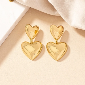 Elegant gold double heart drop earrings with a polished metallic finish on beige texture