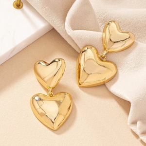 Close-up of golden double-layered heart earrings with a polished mirror finish on fabric