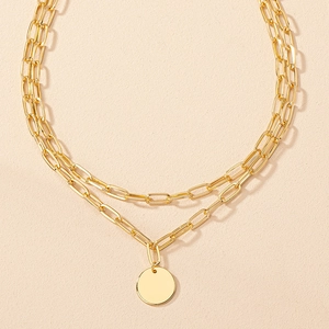 Detail of a gold double-layered chain necklace featuring a minimalist round pendant charm