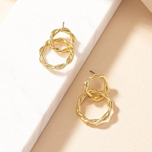 Detailed close-up of golden interlocking twisted hoop earrings on marble texture background
