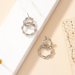 Close-up of silver geometric twisted rope earrings on a white marble background