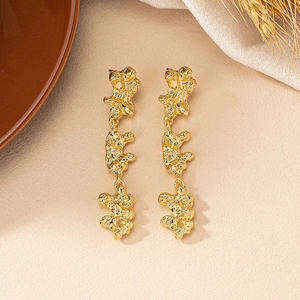 Detailed close-up of long gold-plated drop earrings with irregular molten lava textures